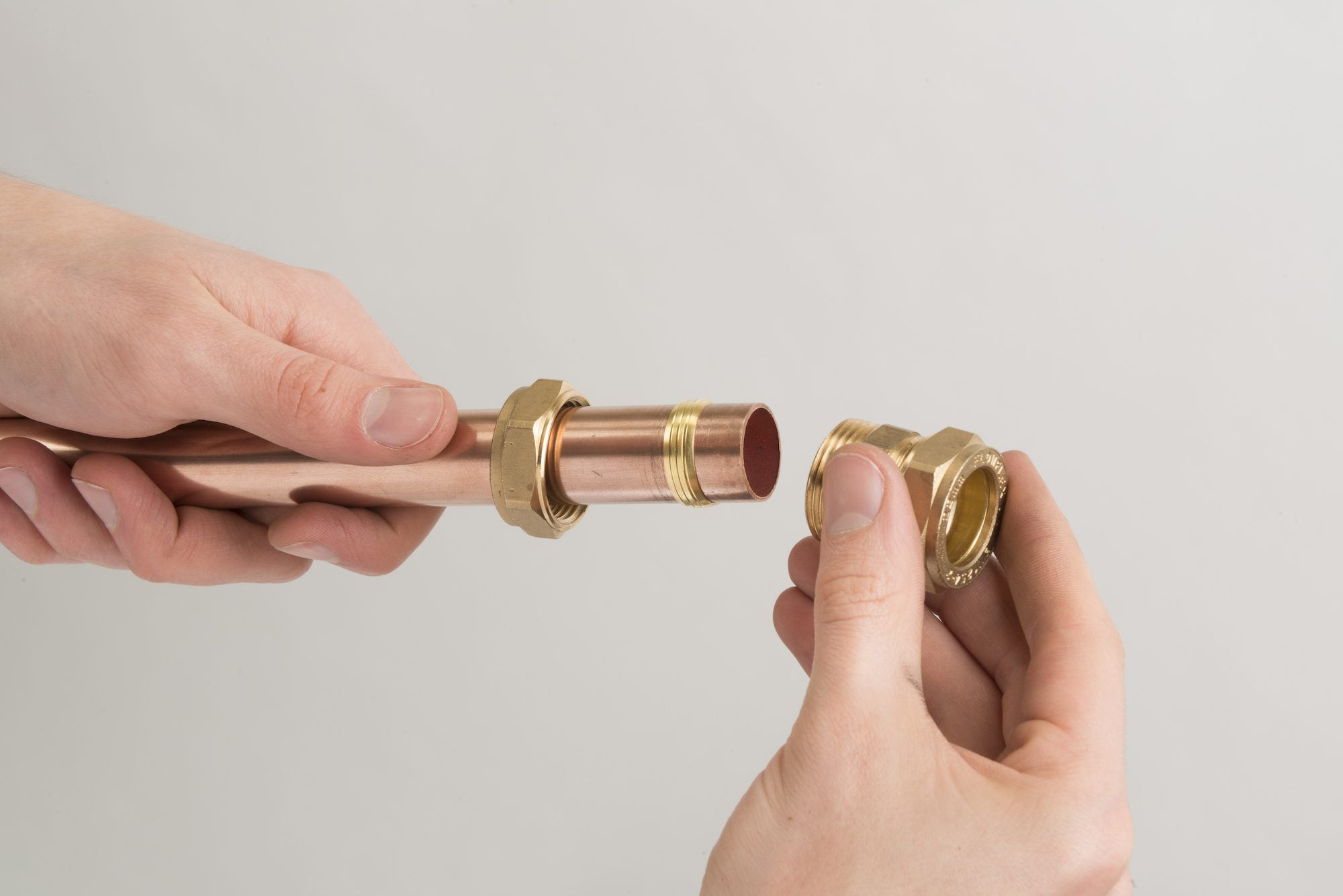 Hands assembling a brass compression fitting onto a copper pipe.