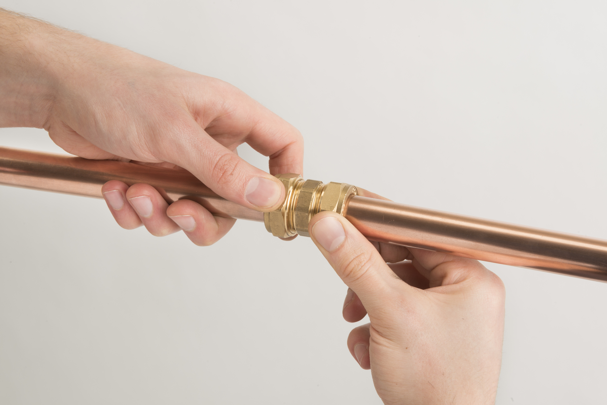 Hands supporting an assembled brass compression coupling on a copper pipe.