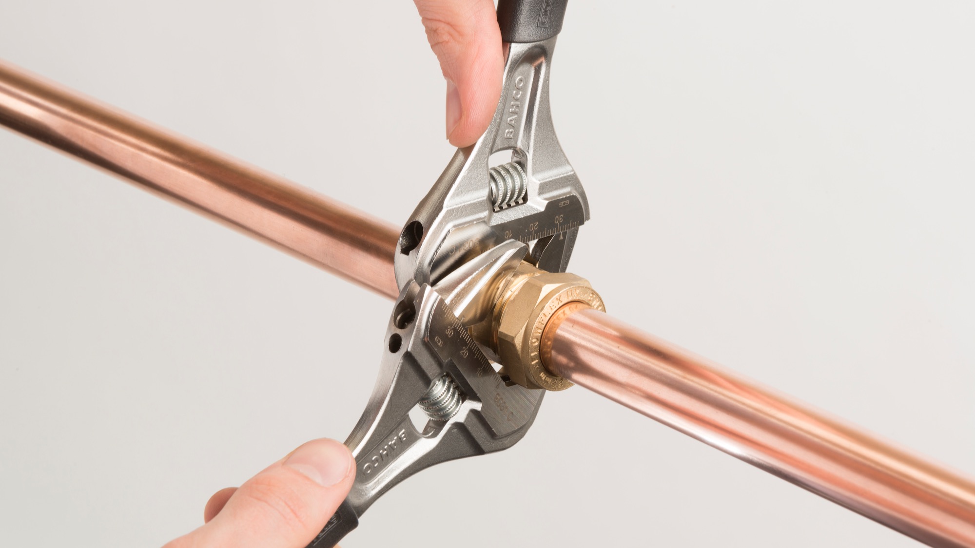 Two adjustable spanners tightening a brass compression coupling on copper pipe.