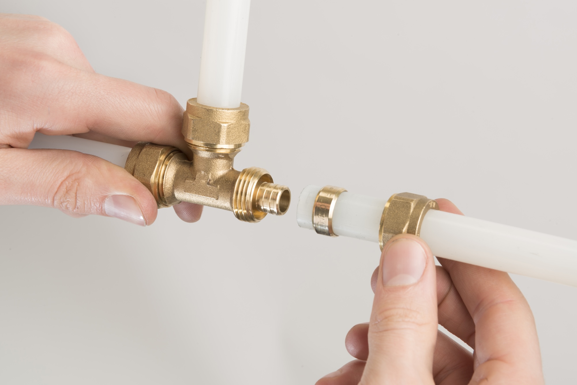 Hands connecting white PEX pipe to a brass compression tee fitting.