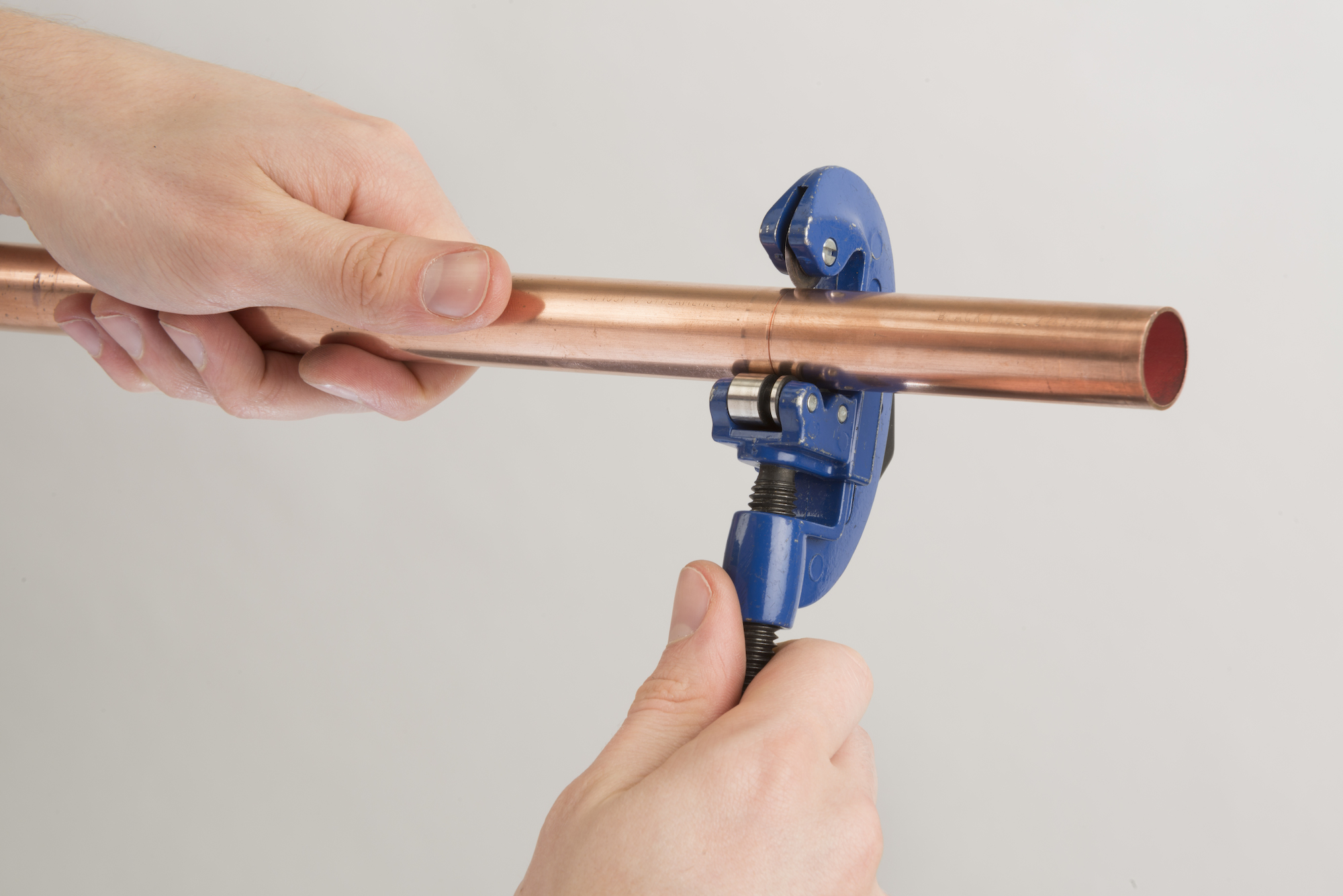 Hands using a blue pipe cutter to cut a length of copper pipe.
