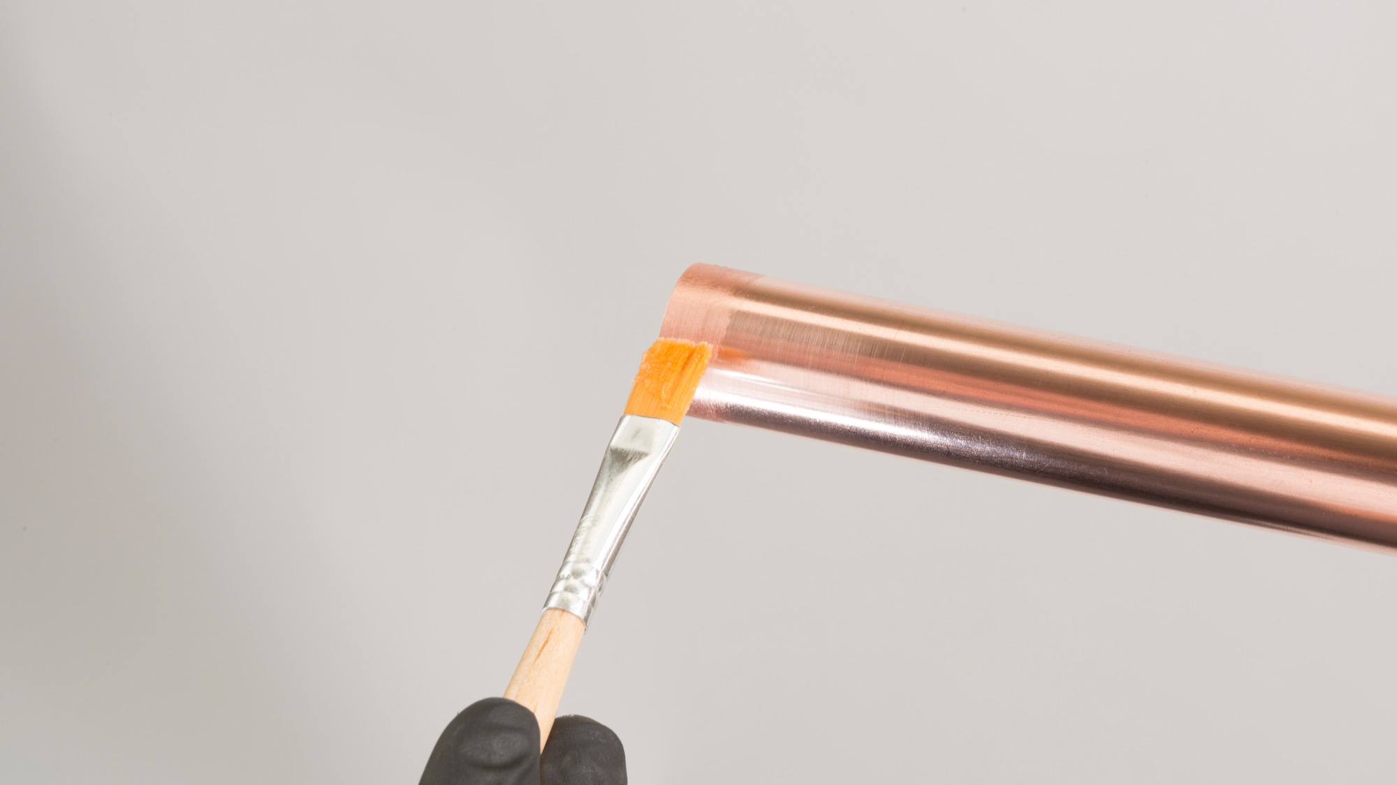 Gloved hand applying flux to the end of a copper pipe before fitting and soldering.