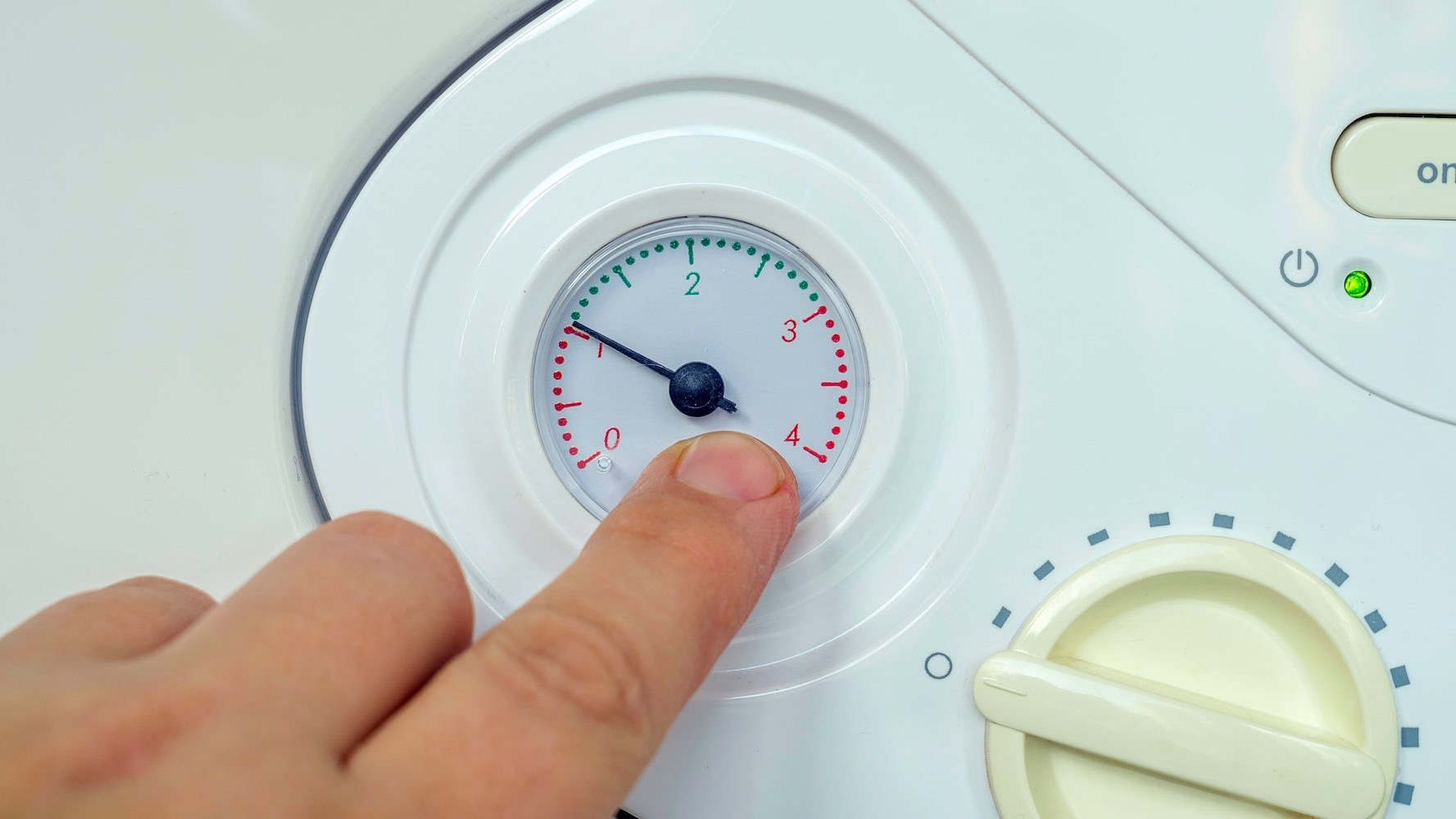 Close-up of a hand pointing at the pressure gauge on a domestic boiler, showing the system pressure within the recommended operating range.