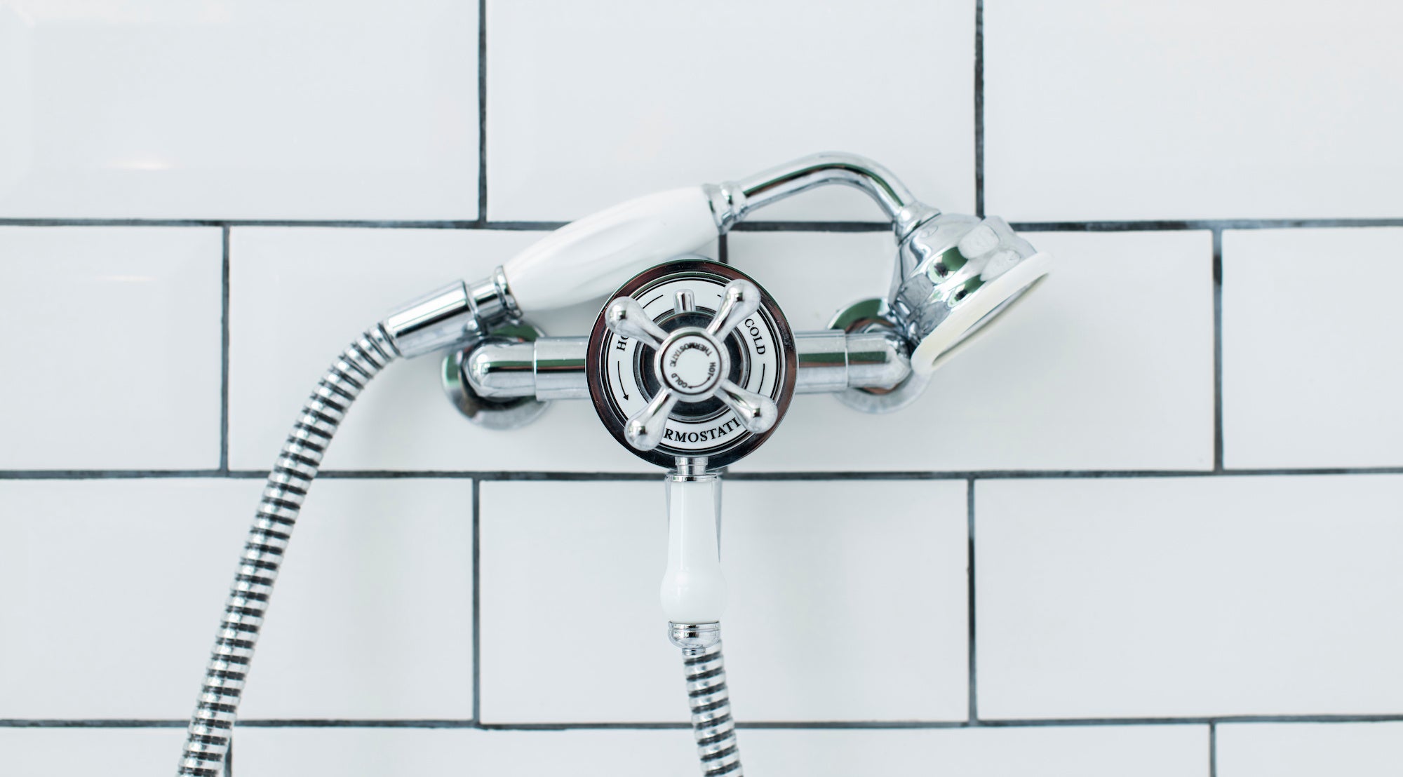 Traditional exposed thermostatic shower mixer with crosshead controls and a handheld shower head mounted on a tiled bathroom wall.